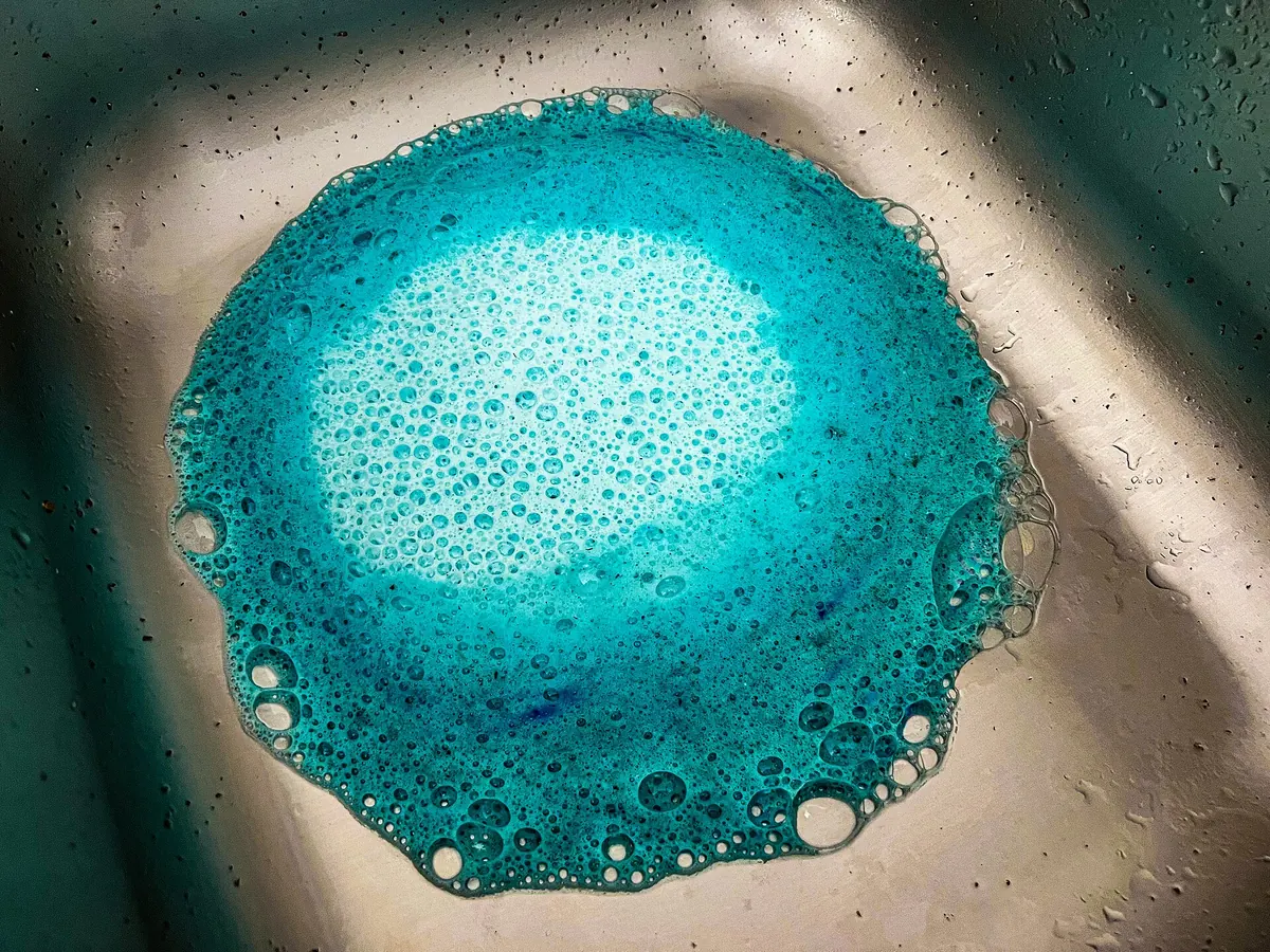 Blue foam bubbling up from a stainless kitchen sink drain