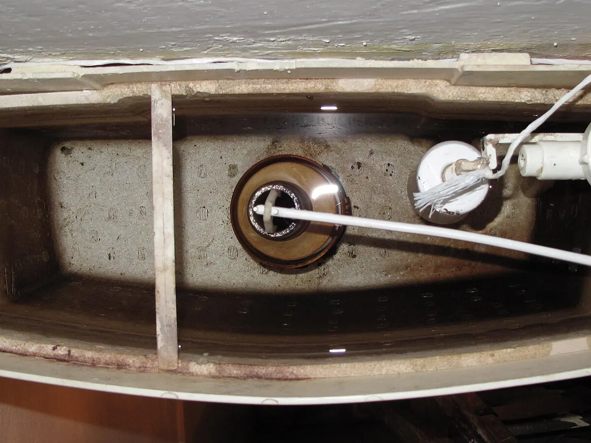 Top view into an open toilet tank with a fill valve, float and flush valve, stained by mineral deposits